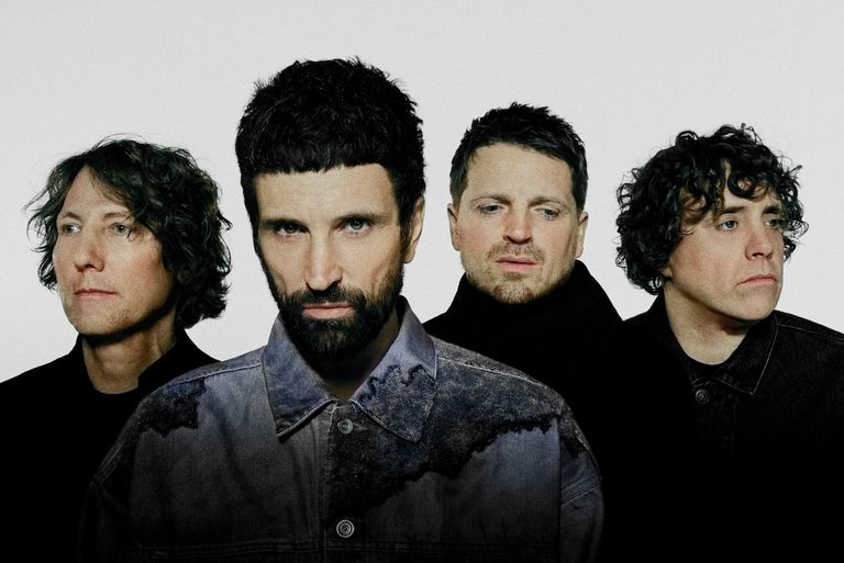 English rock band Kasabian members posing in a close-up group portrait against a plain light grey background.